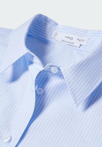 Camisa a rayas azul claro con corte regular, que presenta un cuello con puntas, dos cierres de botón y una textura de tela de algodón suave.