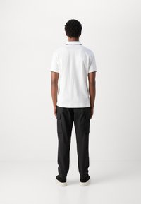 Maglietta polo bianca con bordi neri, abbinata a pantaloni cargo neri. Il tessuto appare liscio e il design è informale con una vestibilità comoda.