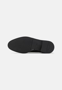 Semelle de chaussure habillée en cuir noir avec couture subtile, avant texturé, milieu lisse et nom de marque embossé près de la voûte.