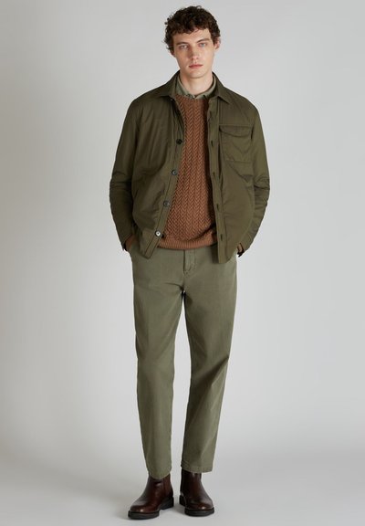 Giacca leggera verde oliva, maglione lavorato a maglia marrone, pantaloni oliva, stivali in pelle marrone e una camicia con colletto. Design semplice, accenti minimi.