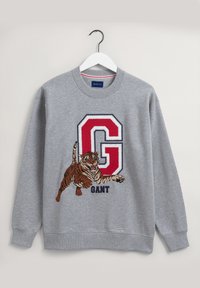 Sudadera gris con un tigre bordado y un gran emblema "G" rojo. Tela suave, cuello redondo y puños acanalados. Etiqueta de la marca: GANT.