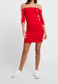 Red off-the-shoulder dress made of stretchy fabric, featuring three white stripes along the sleeves and a small logo on the chest.