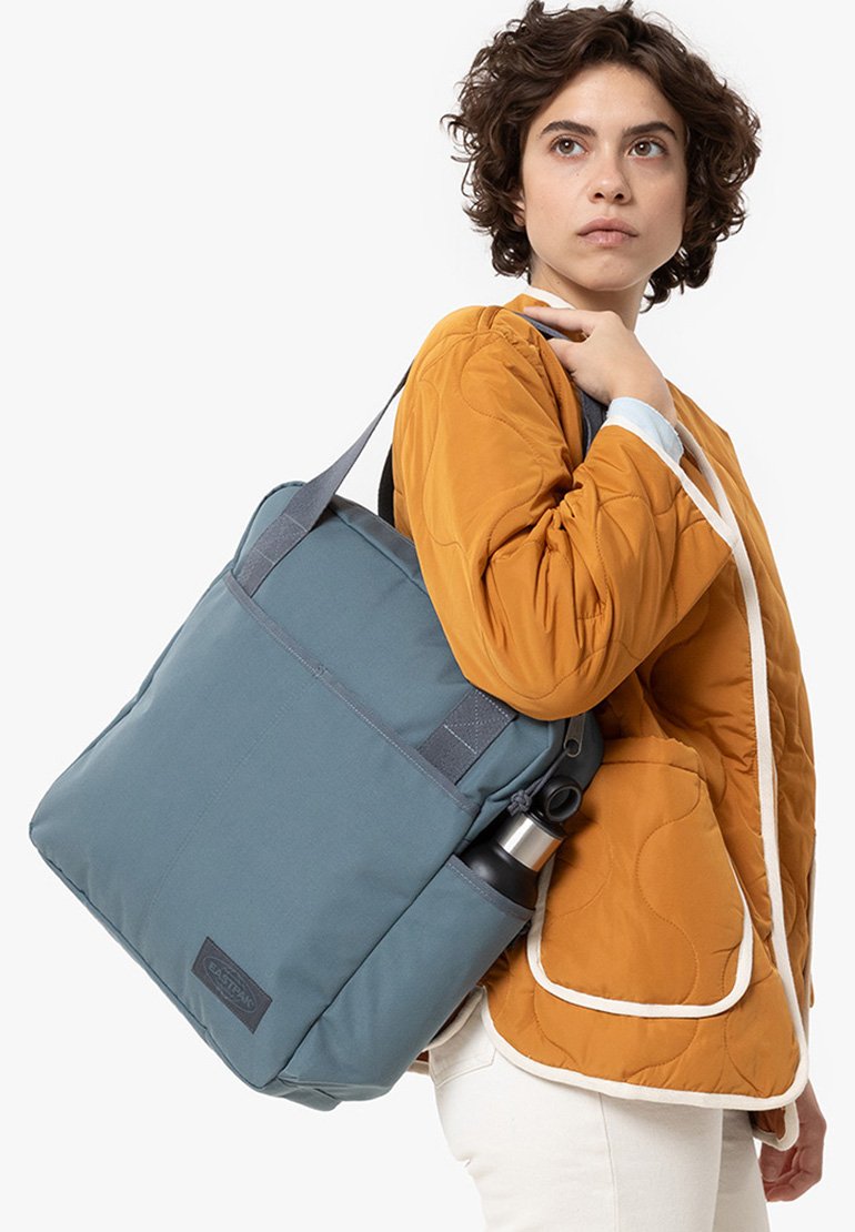 Borsa a tracolla grigio-blu con spallacci regolabili, forma rettangolare e una tasca laterale per una bottiglia d'acqua. Realizzata in tessuto resistente.