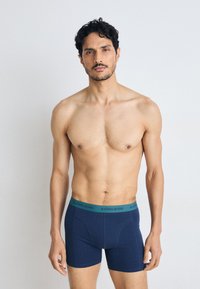 Sötétkék pamut boxer alsónadrág zöld derékkal, amelyen a "BJÖRN BORG" logó található. Testhez simuló kialakítás, sima textúra, combközép hosszúság.