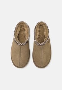 Bruna mockasiner i mocka med en mjuk, fluffig foder och dekorativ flätad kant längs kragen. Rund tå och platt sula.