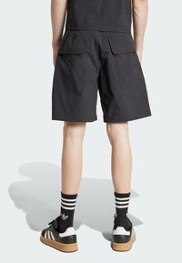 Čierne kraťasy s voľným strihom, dvojitými zadnými vreckami a hladkou textúrou, skombinované s čierno-bielymi prúžkovanými ponožkami a teniskami.