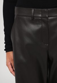 Brune skinnbukser med en jevn tekstur, frontlommer og en tettsittende design. Midjebåndet har en subtil sømdetalj.