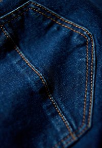 Ciemnoniebieska deninowa tkanina z widocznymi pomarańczowymi szwami na kieszeni. Tekstura jest gładka z lekkim wyblaknięciem w niektórych miejscach.