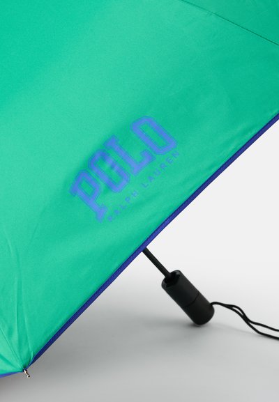Zöld ernyő kék díszítéssel és fogantyúval. A napernyőn kék "POLO RALPH LAUREN" logó található, kiemelve a sima szövet textúráját.