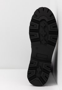 Suela de zapato de goma negra con un patrón de textura, que presenta surcos profundos y un diseño en cruz para mejorar el agarre y la estabilidad. Talla 37 marcada.