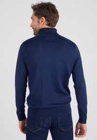 Suéter de punto azul marino con cuello alto, puños de canalé y dobladillo. Presenta una textura suave y un diseño ajustado, combinado con jeans de mezclilla.