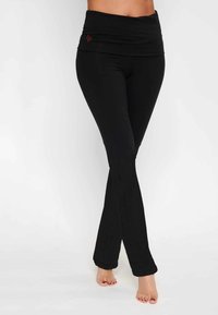 Svarta utsvängda leggings med en bred, vikbar midja, tillverkade av stretchigt tyg. Har en subtil textur och en liten röd broderad logotyp.