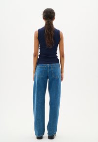 Top senza maniche a coste blu marino abbinato a jeans in denim azzurro chiaro a vita alta e dalla vestibilità ampia, con tasche posteriori rettangolari e cuciture sottili.