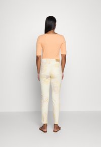 Růžový přiléhavý top s rukávy do lokte, v kombinaci se smetanovými kalhotami s pastelovými květinovými vzory. Celý outfit doplňují jednoduché sandály.