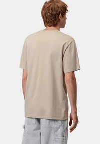 Camiseta de algodón beige con mangas cortas y cuello redondo, con un corte relajado y una textura suave, vista desde la parte de atrás.