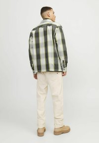 Giacca a quadri in tonalità grigie, verdi e gialle con una vestibilità rilassata, abbinata a pantaloni crema chiaro e scarpe beige. Presenti dettagli con bottoni.
