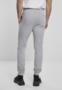 Grå sweatpants med en tapered passform, tillverkade av textil, har sidofickor och elastiska mudd. Svarta sneakers kompletterar looken.