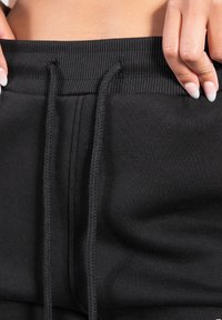 Svarta bomullsjoggers med en ribbad midjeband och justerbara dragsnören, med en slät textur och minimalistisk design.