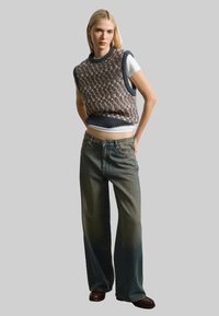 Chaleco de punto en tonos marrones y azules, con un patrón texturizado, combinado con unos pantalones vaqueros de pierna ancha de cintura alta en azul claro y zapatos marrones oscuros.