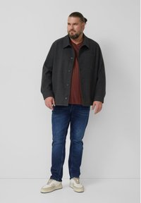 Wełniana, węglowoszara kurtka z zapięciem na guziki, kieszenią na piersi i kołnierzem, noszona na bordowej koszuli i niebieskich dżinsach.