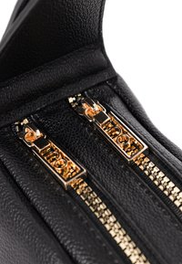 Schwarze Ledertasche mit zwei goldenen Reißverschlüssen und strukturiertem Oberflächen. Die Reißverschlüsse verfügen über horizontale Gravuren, die ein elegantes Design umreißen.