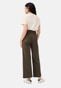Weite, olivgrüne Hose aus Baumwolle mit hoher Taille, ausgestattet mit zwei Gesäßtaschen und gesäumten Bündchen. Getragen mit einem cremefarbenen T-Shirt und Sneakers.