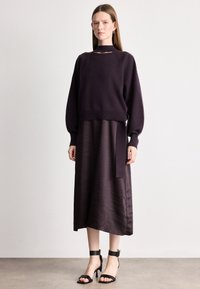 Tamno ljubičasti pleteni pulover s izrezom, uparen s odgovarajućom midi suknjom s bočnim vezanjem, upotpunjen crnim sandalama s potpeticom.