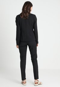 Černý oblek na míru, slim fit, s klopovým blejzrem a rovnými kalhotami. Vyrobeno z hladké tkaniny s knoflíkovými akcenty.
