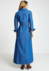 Maxikleid aus Denim in Blau mit langen Ärmeln, Kragen und tailliertem Gürtel. Verfügt über einen geraden Schnitt und dekorative Manschetten.