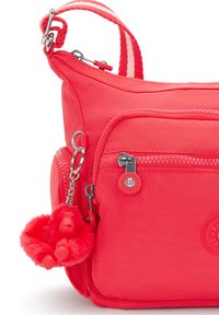 Rote Nylon-Crossbody-Tasche mit mehreren Reißverschlussfächern, gestreiftem Schulterriemen und einem flauschigen roten Affen-Schlüsselanhänger, der angebracht ist.