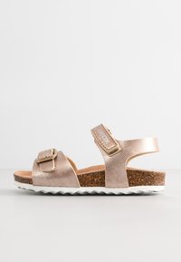 Metalen roségouden sandaal met twee banden, kurken voetbed en een witte rubberen buitenzool met een zigzagpatroon. Verstelbare gespsluiting.