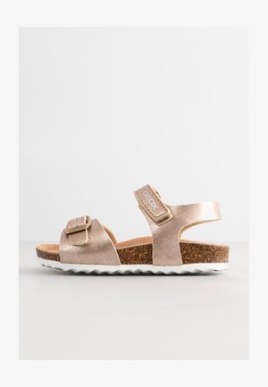 Metallic rose gold sandal with two straps, cork footbed, and white rubber outsole featuring a zigzag pattern. Adjustable buckle detail.