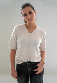 Pull léger en maille blanche à manches courtes et décolleté en V, associé à un jean foncé ajusté. Les accessoires comprennent une montre en or et des bagues.