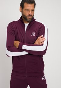 Chándal deportivo burdeos con detalles blancos, chaqueta con cremallera y pantalones a juego. Presenta un logo en el pecho y paneles de manga texturizados.