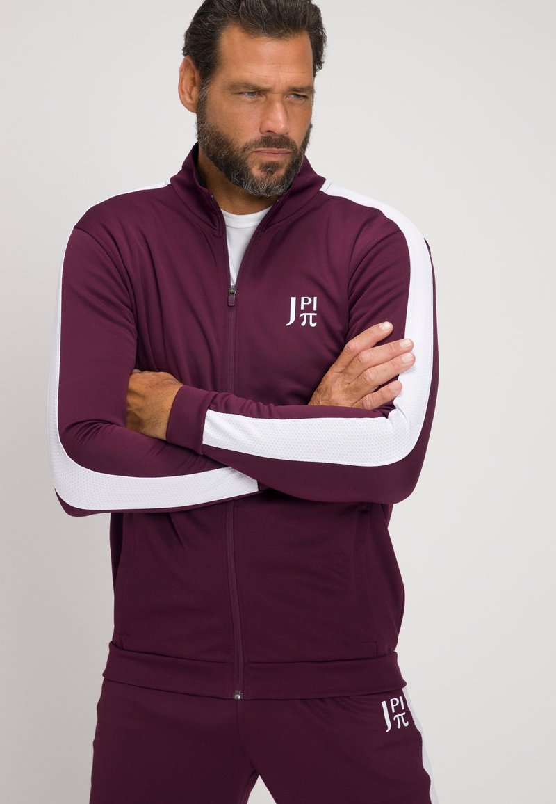 Maroon Sportanzug mit weißen Akzenten, zip-fähige Jacke und passender Hose. Merkmale ein Logo auf der Brust und strukturierte Ärmelpaneele.