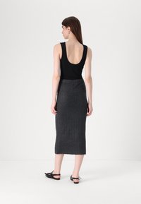 Top negru fără mâneci, cu spate în formă de U, asortat cu o fustă lungă, gri, cu textură ribbed. Modelul poartă pantofi negri fără toc, cu detalii sub formă de fundiță.