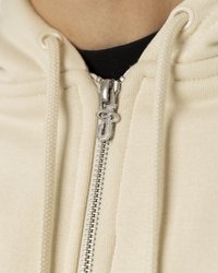 Krém színű kapucnis felöltő, ezüst cipzárral, jellegzetes hardverrel és fonott szövet textúrával a cipzár környékén.