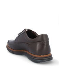 Zapato de cuero marrón con punta redondeada, diseño con cordones y suela contrastante en color beige. Presenta una textura suave y detalles de costura mínimos.