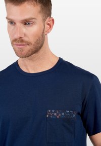 Mörkblå bomulls T-shirt med rund hals och bröstficka som har en blommig tygdetalj i blå, röd och gul mönster.