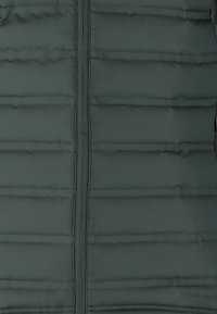 Mørkegrøn puffjakke med vandret quiltning, en fuld lynlås foran og ordet "ENDURANCE" diskret trykt på siden.