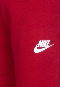 Piros pamut melegítőnadrág, amely puha tapintású, az oldalon fehér Nike logóval. A dizájn egyszerű, további minták nélkül.