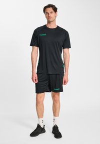 Czarna koszulka sportowa i spodenki wykonane z lekkiego materiału. Z zielonymi akcentami i logo. Uzupełnione czarnymi butami i białymi skarpetkami.