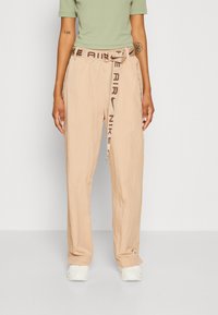 Beige cargo kalhoty s texturovaným povrchem, s hnědým opaskem s logem "NIKE AIR" a bočními kapsami, doplněné bílými teniskami.