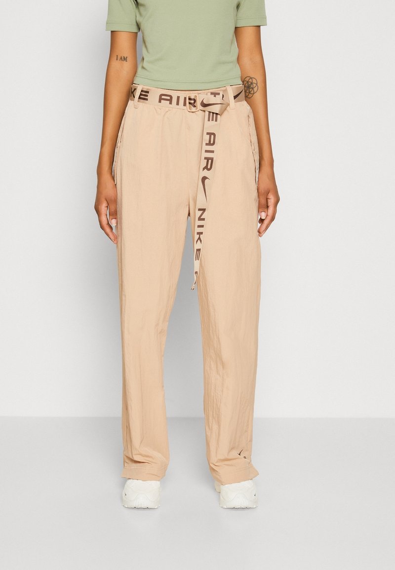 Beige cargo kalhoty s texturovaným povrchem, s hnědým opaskem s logem "NIKE AIR" a bočními kapsami, doplněné bílými teniskami.