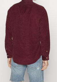 Burgundská košile z manšestrové látky s límečkem na knoflíky, dlouhými rukávy a knoflíkovými manžetami, s zúženým zadním lemem a texturovanou látkou.