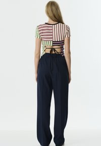 Veelkleurige gestreepte top met korte mouwen en strik aan de achterkant, gecombineerd met losse marineblauwe wijde broek met een elastische tailleband.