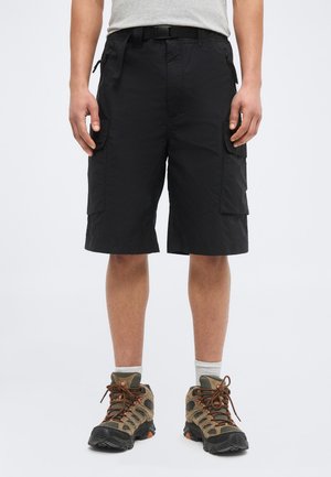 Adult wearing black cargo shorts, gray socks, and brown hiking shoes, standing with hands relaxed by sides against a plain background.