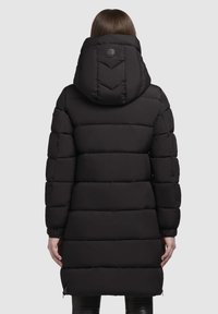 Abrigo acolchado negro con capucha, que presenta un diseño acolchado horizontal, puños elásticos y una insignia con logo en la parte posterior. Cierre con cremallera en el dobladillo.