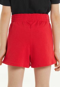 Shorts en coton rouge avec une large ceinture élastique, présentant une texture lisse et une coupe droite, finie par un bord ourlé.