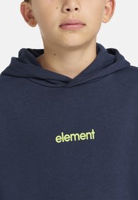 Mörkblå hoodie i bomull, med en känguruficka och en limegrön "element"-logotyp på bröstet, samt en justerbar huva.